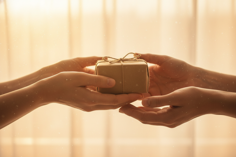 Two hands offering a small kraft-paper gift box

Another pair of hands reaching out to receive it

Cropped at the wrists — no faces, just hands and emotion

Soft morning sunlight in the background

Mood: warm, sincere, a little magical
